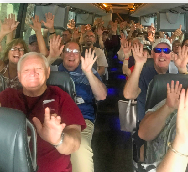 Smiling group of people with their hands up in the air inside a motorcoach tour bus