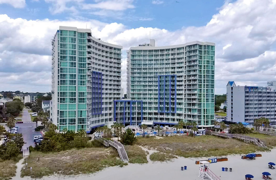 An exterior view of an oceanfront resort, blue cloudy sky and beach