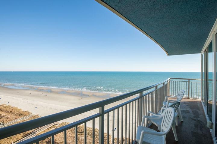 picture of an oceanfront balcony of a condo at avista resort showing the ocean, sand, blue skies and white chairs to enjoy relaxing in.