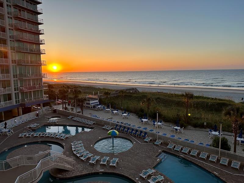 Sunset at Avista Resort with pools in front and the ocean beyond under an orange sky.
