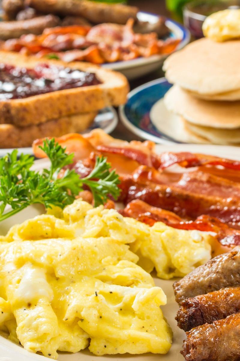 Assortment of breakfast items including sausage links, scrambled eggs, bacon, toast with jelly, and pancakes.