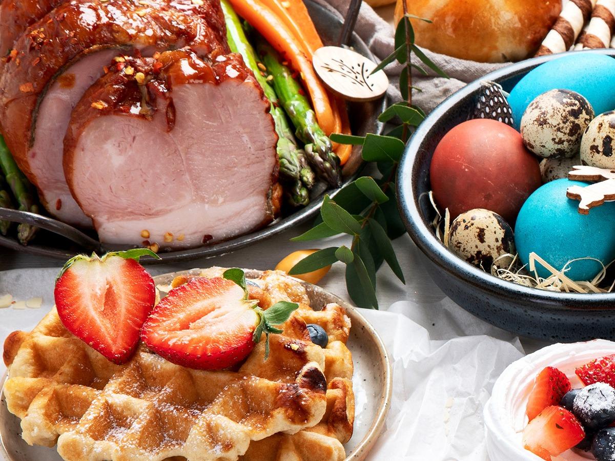 A table prepped with an Easter dinner including ham, strawberries and colored eggs
