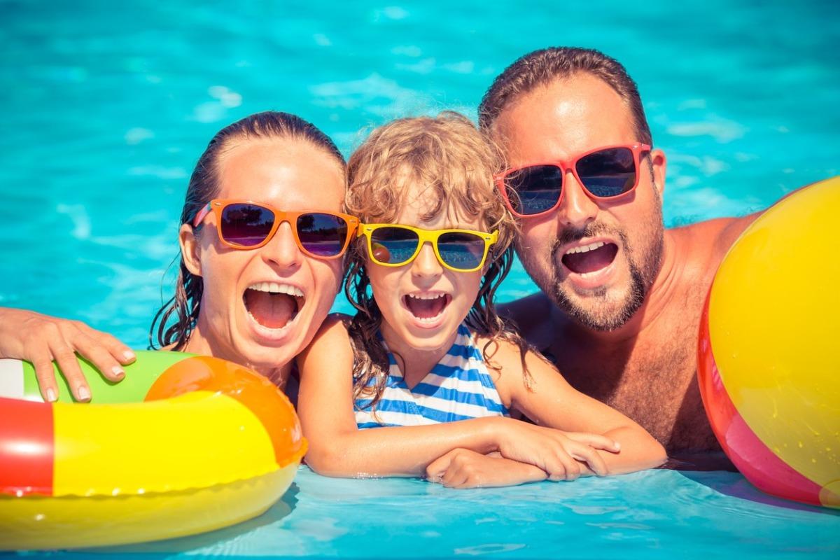 mom, dad and kid in a pool with floats at the beach all wearing sunglasses and smiling