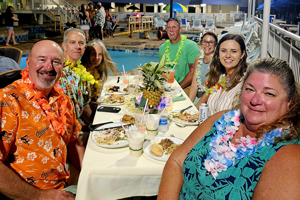 Group of smiling people wearing hawaiian leis at an outdoor table