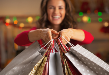 A smiling woman holding shopping bags up to the camera.