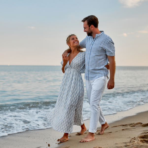 a smiling couple walking on the beach wearing striped outfits