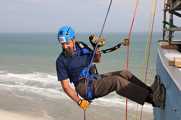 Person wearing a safety hat rappelling over the side of a high rise building with the beach and ocean in the background