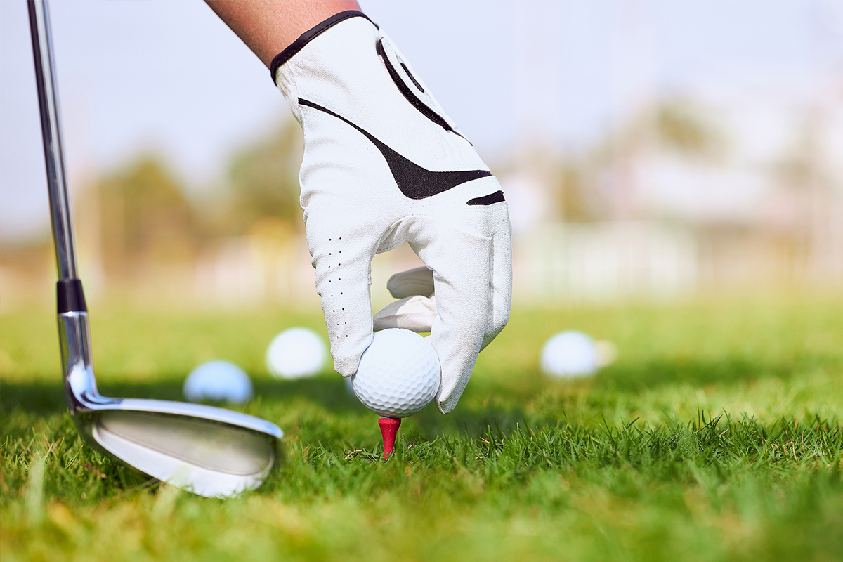 A hand gripping a golf club and ball, ready for a swing on a golf course.