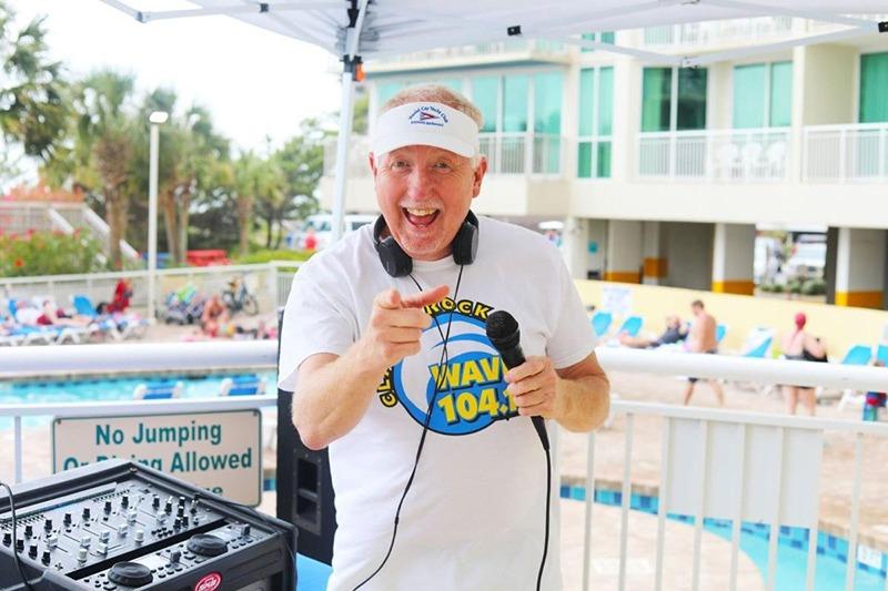 Smiling Disc Jockey with equipment standing outdoors at the Avista Resort pool