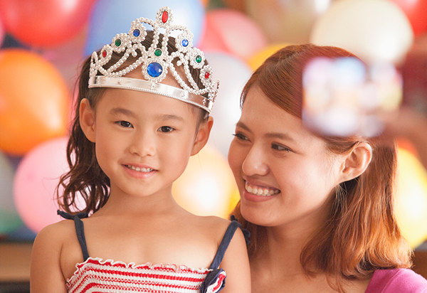 woman and small child wearing a tiara with a colorful balloon background