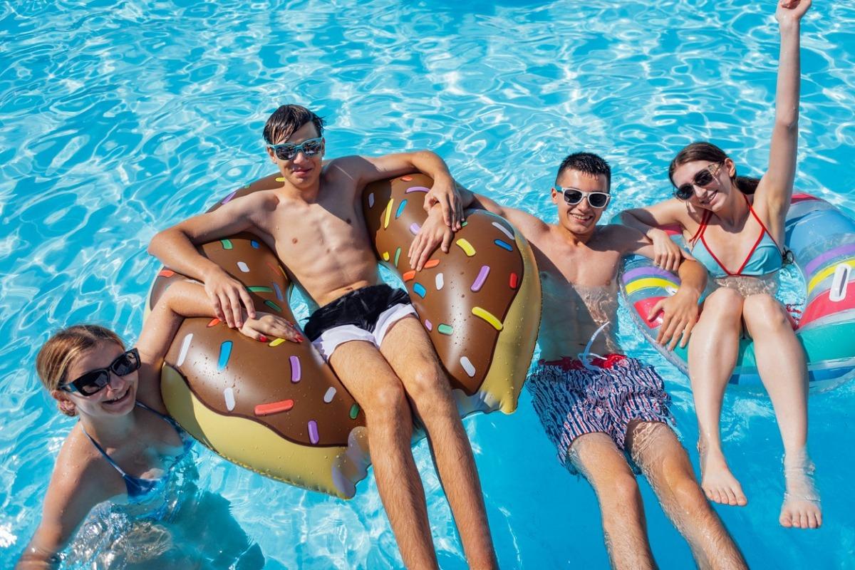 4 teenagers two on pool floats and two in water of a pool