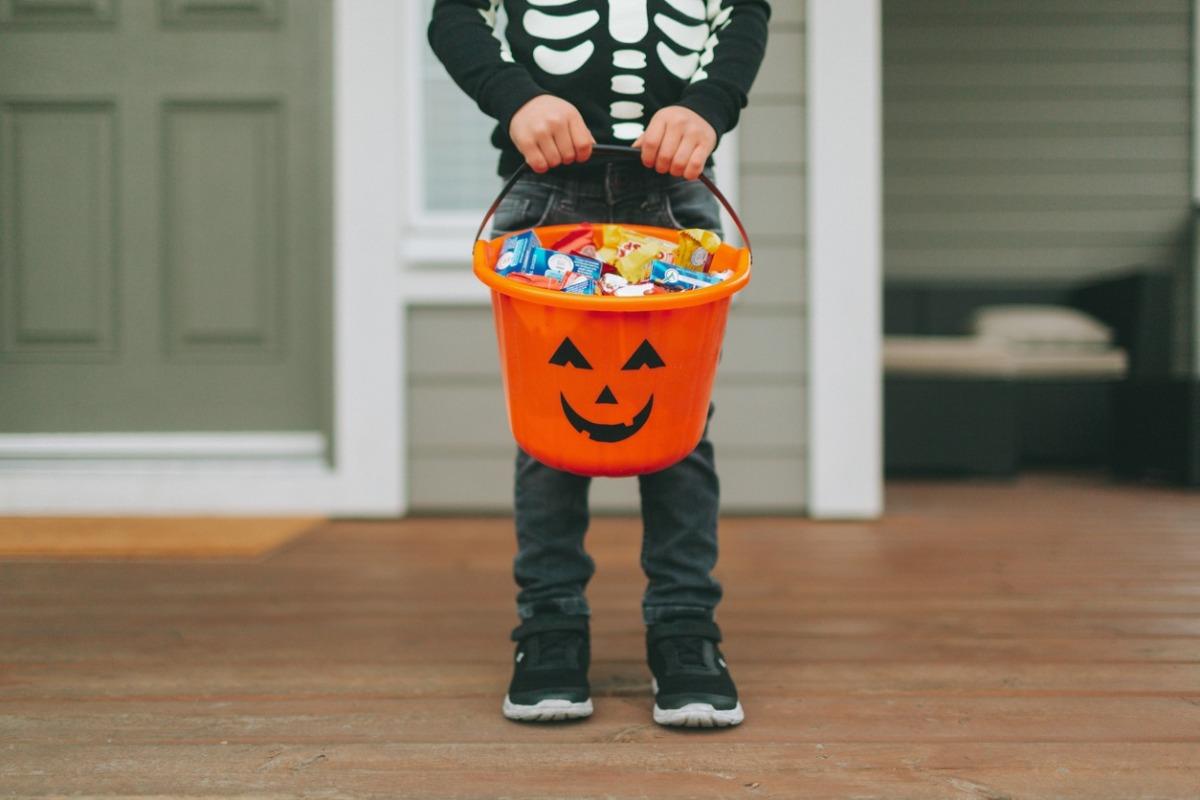 Low Section Of Boy With Sweet Food In Bucket Standing At Home During Halloween
