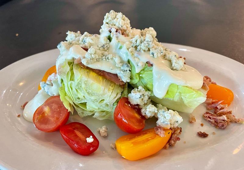 Wedge salad with iceberg, tomatoes, crumbled blue cheese and bacon on a white plate at Avista Resort's onsite restaurant Just Off Main
