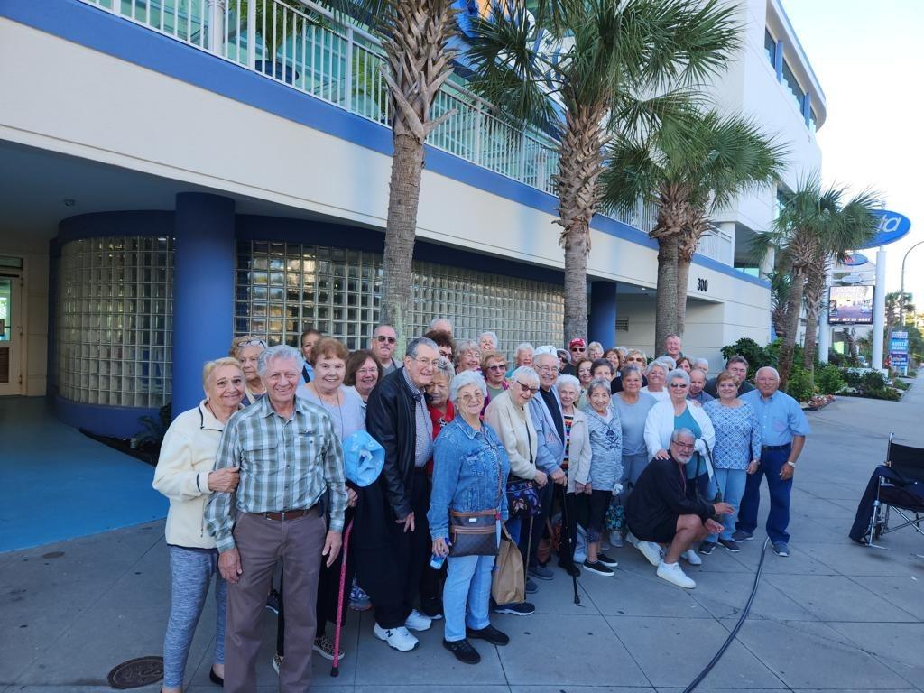 Group of smiling seniors posing together outside the Avista Resort with palm trees