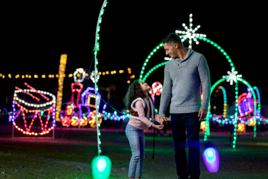 Father and daughter enjoying a colorful outdoor holiday lights display.